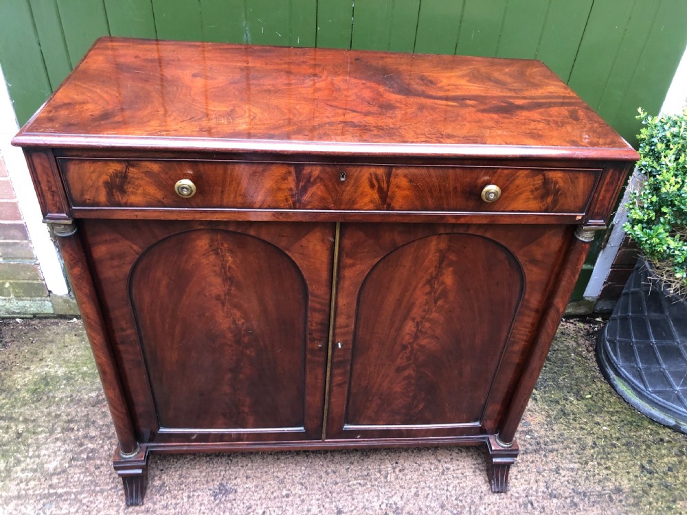 An early nineteenth-century flame mahogany side cabinet with arch-panelled double doors, top drawer, and brass fittings. View VI