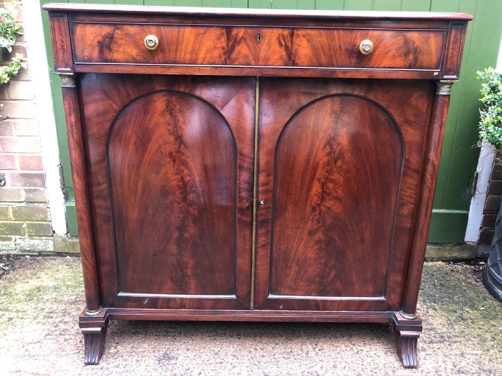 An early nineteenth-century flame mahogany side cabinet with arch-panelled double doors, top drawer, and brass fittings. View IX