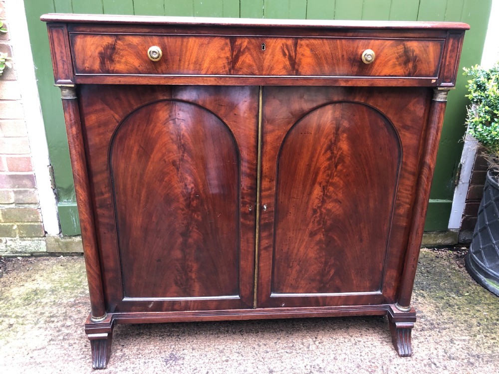 An early nineteenth-century flame mahogany side cabinet with arch-panelled double doors, top drawer, and brass fittings. View X