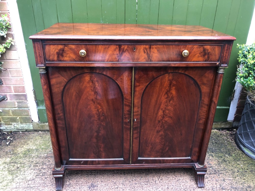 An early nineteenth-century flame mahogany side cabinet with arch-panelled double doors, top drawer, and brass fittings. View XI