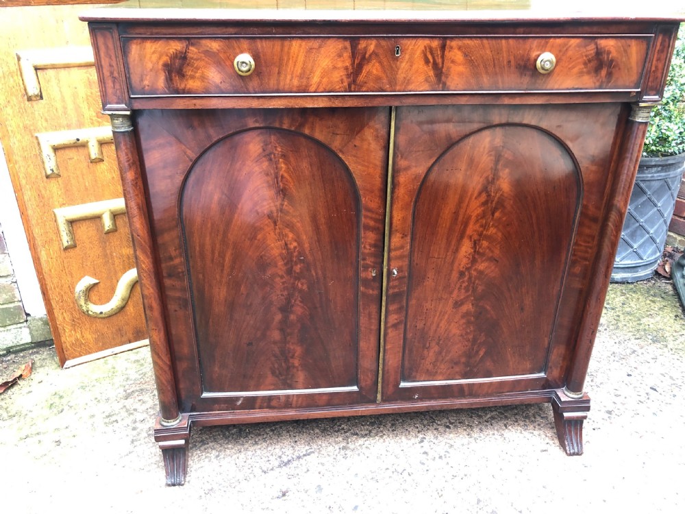 An early nineteenth-century flame mahogany side cabinet with arch-panelled double doors, top drawer, and brass fittings. View XII