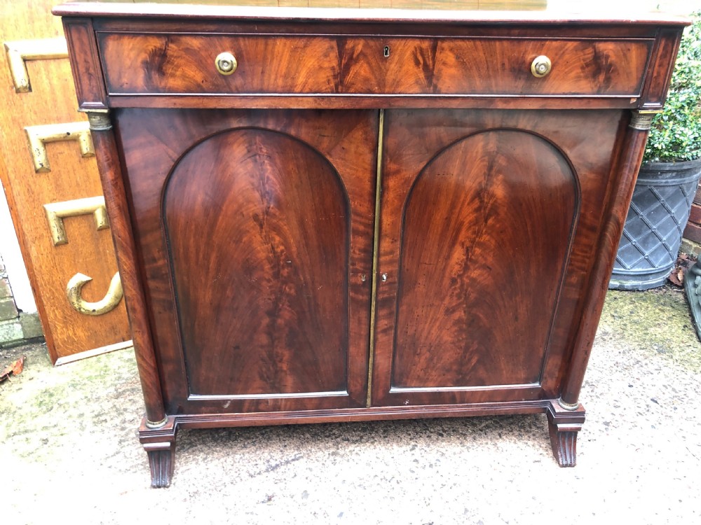 An early nineteenth-century flame mahogany side cabinet with arch-panelled double doors, top drawer, and brass fittings. View XV