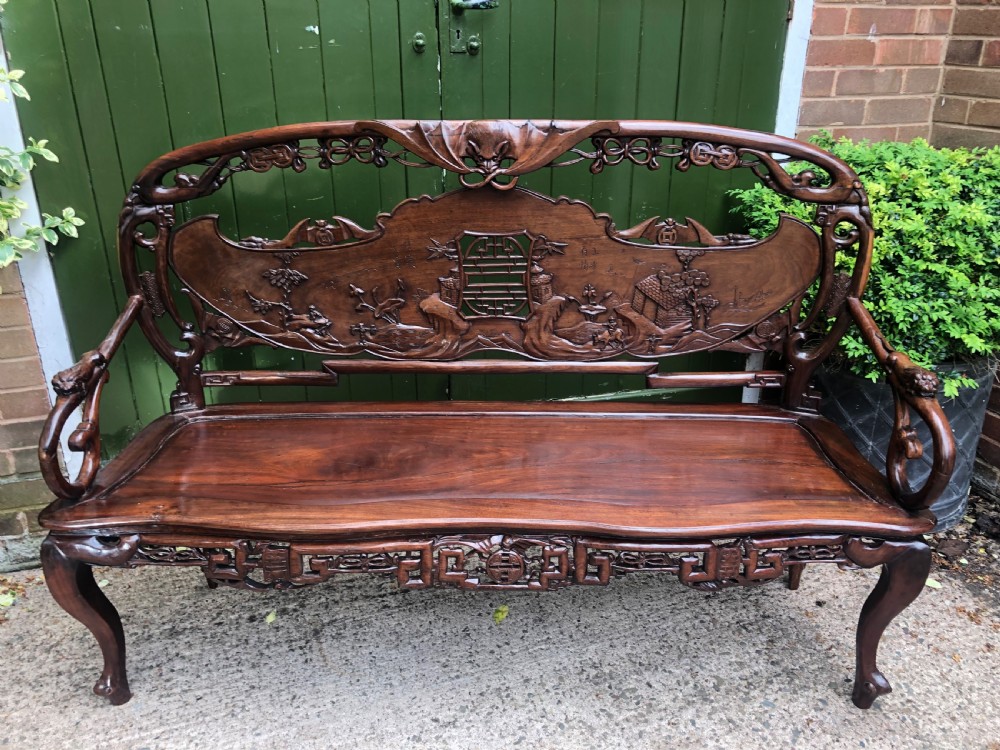 An antique Chinese dark hardwood hall bench featuring detailed relief carvings of bats, landscapes, and traditional character motifs on the backrest. View II