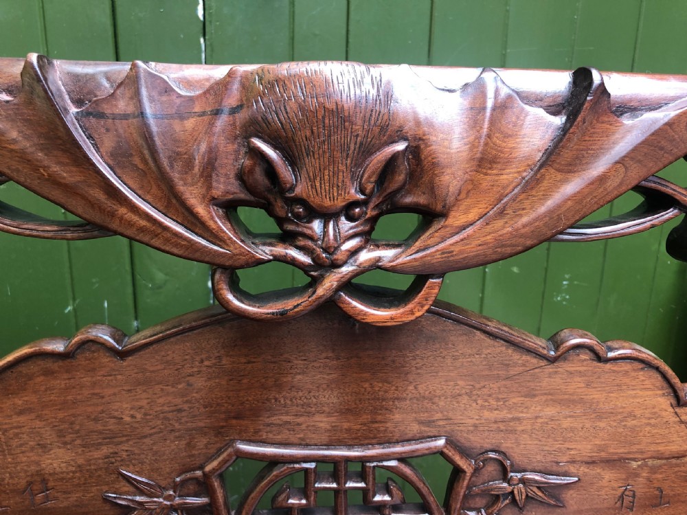 An antique Chinese dark hardwood hall bench featuring detailed relief carvings of bats, landscapes, and traditional character motifs on the backrest. View VI