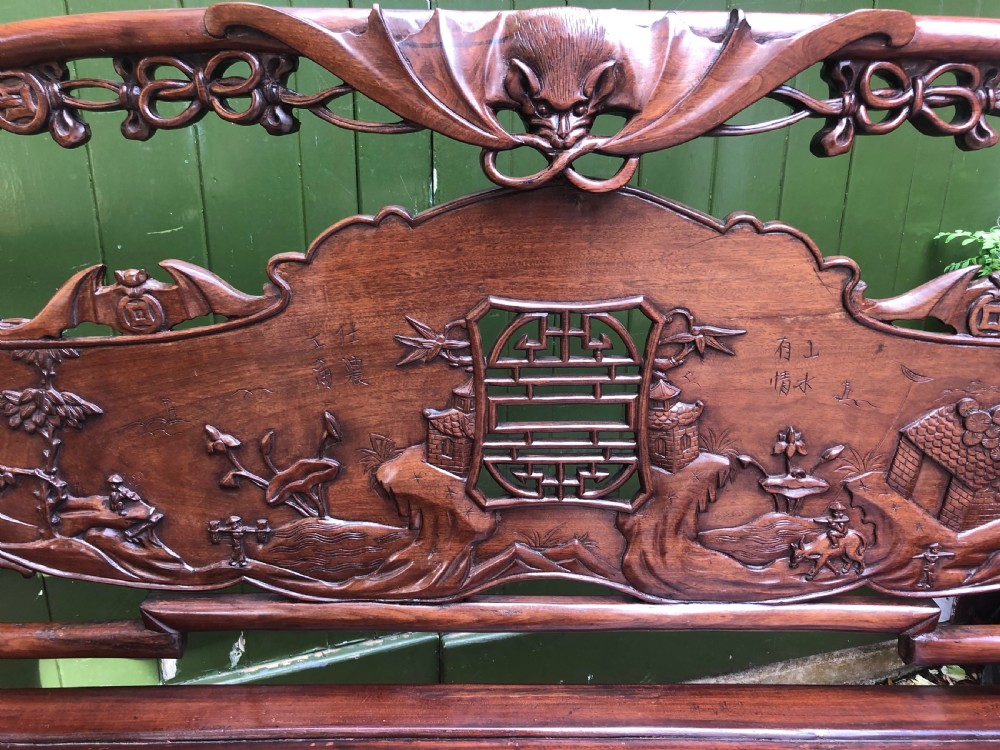 An antique Chinese dark hardwood hall bench featuring detailed relief carvings of bats, landscapes, and traditional character motifs on the backrest. View VII