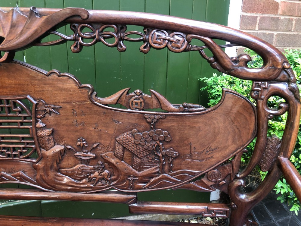 An antique Chinese dark hardwood hall bench featuring detailed relief carvings of bats, landscapes, and traditional character motifs on the backrest. View VIII
