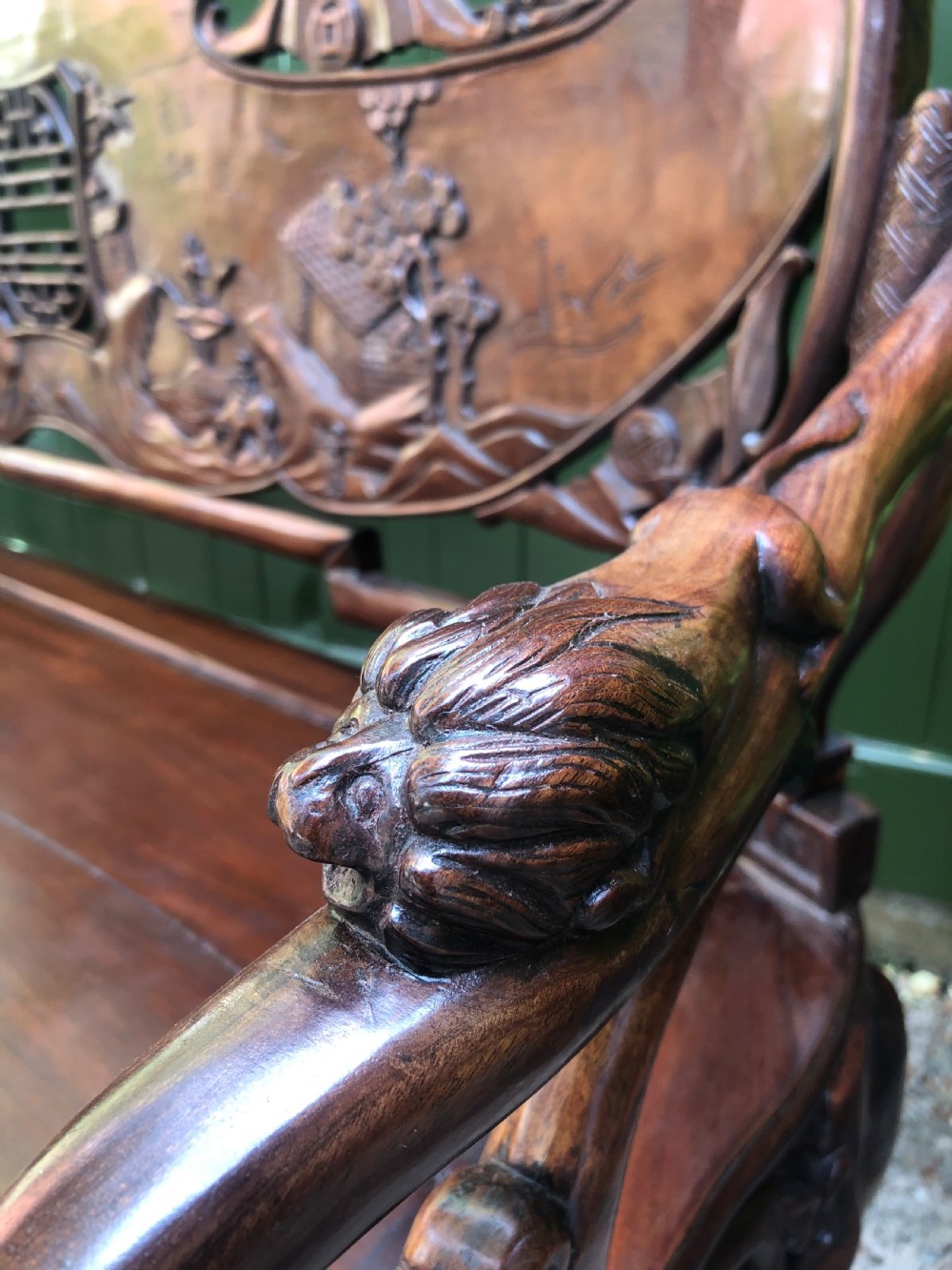 An antique Chinese dark hardwood hall bench featuring detailed relief carvings of bats, landscapes, and traditional character motifs on the backrest. View IX