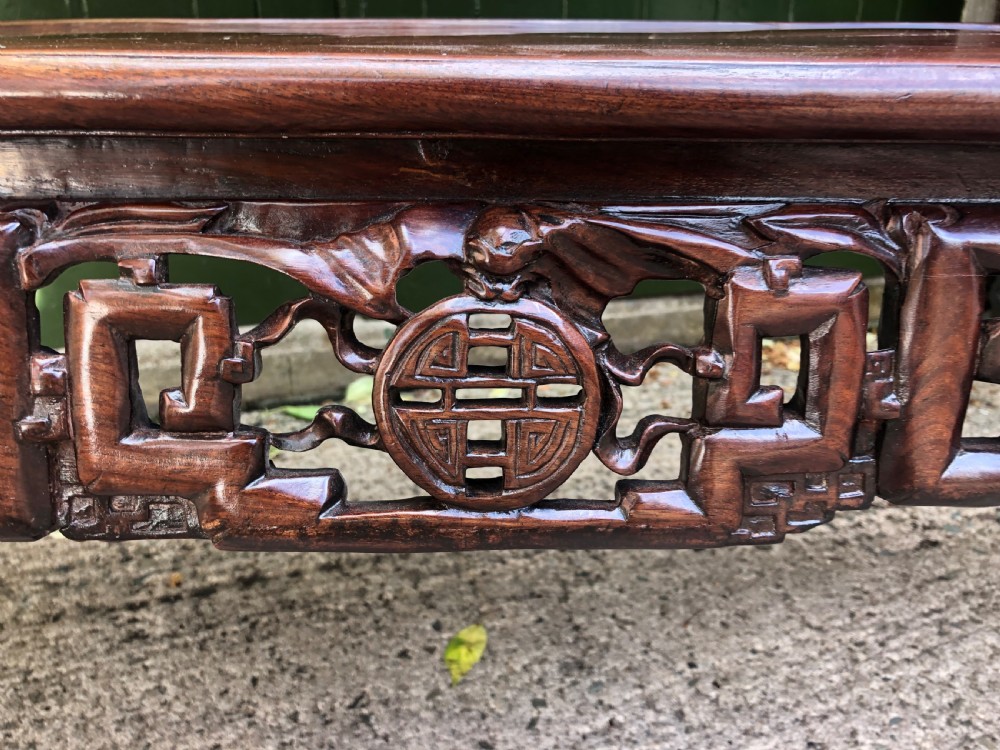 An antique Chinese dark hardwood hall bench featuring detailed relief carvings of bats, landscapes, and traditional character motifs on the backrest. View X