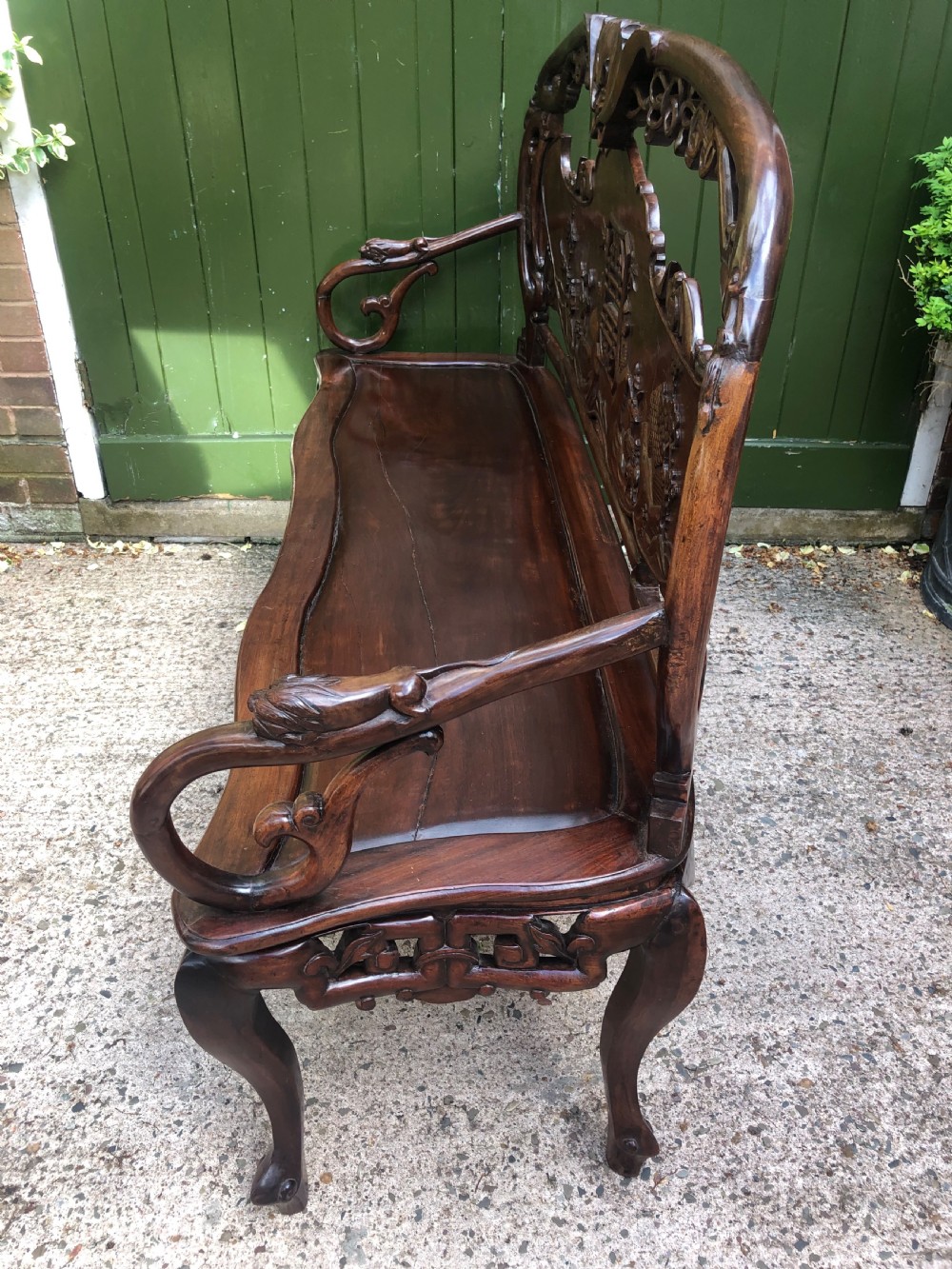 An antique Chinese dark hardwood hall bench featuring detailed relief carvings of bats, landscapes, and traditional character motifs on the backrest. View XVII