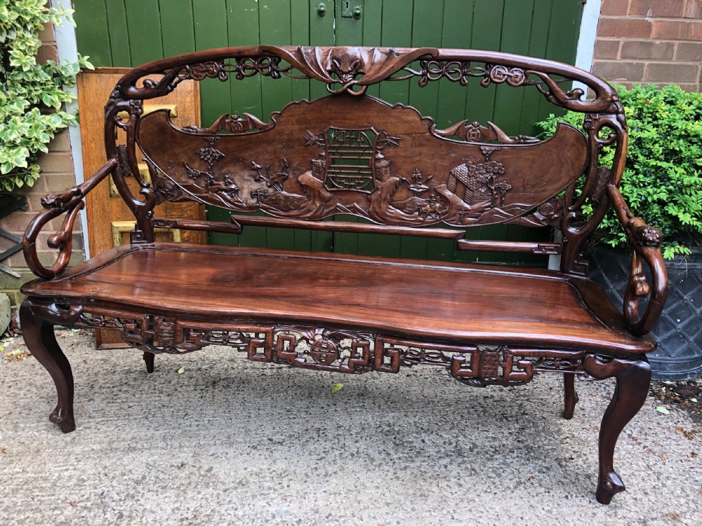 An antique Chinese dark hardwood hall bench featuring detailed relief carvings of bats, landscapes, and traditional character motifs on the backrest. View XIX