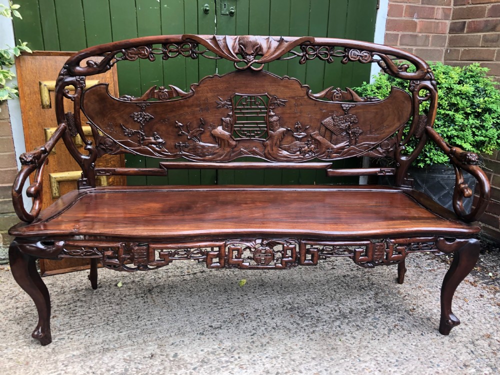 An antique Chinese dark hardwood hall bench featuring detailed relief carvings of bats, landscapes, and traditional character motifs on the backrest. View XXI