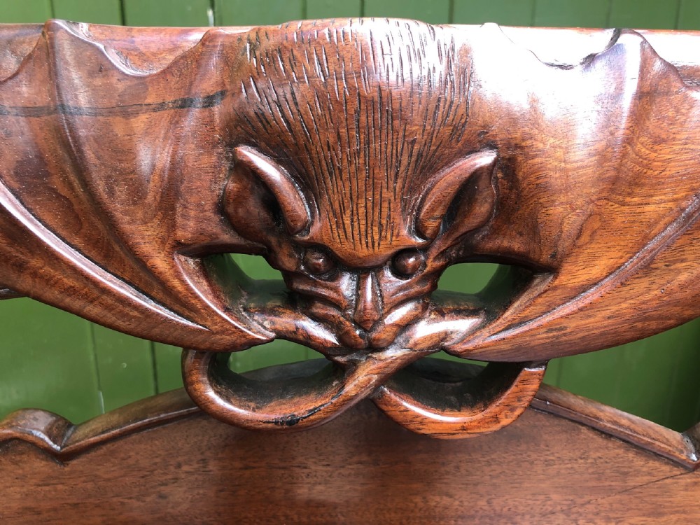 An antique Chinese dark hardwood hall bench featuring detailed relief carvings of bats, landscapes, and traditional character motifs on the backrest. View XXII