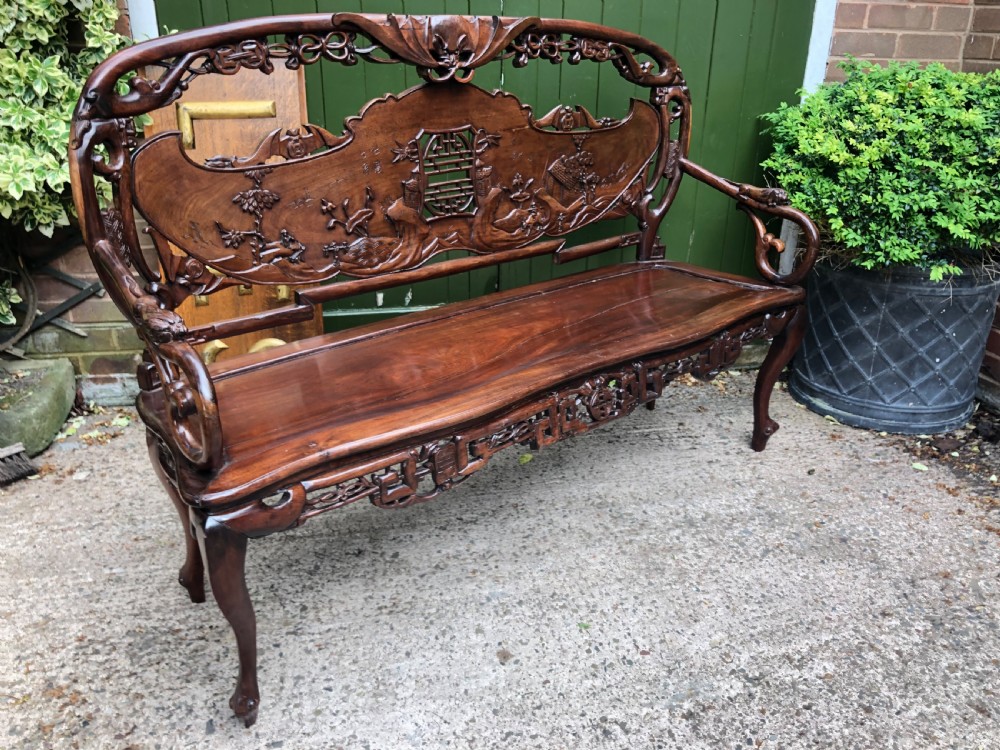 An antique Chinese dark hardwood hall bench featuring detailed relief carvings of bats, landscapes, and traditional character motifs on the backrest. View XXV