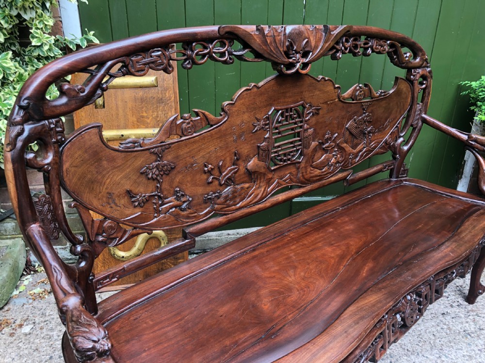 An antique Chinese dark hardwood hall bench featuring detailed relief carvings of bats, landscapes, and traditional character motifs on the backrest. View XXVI