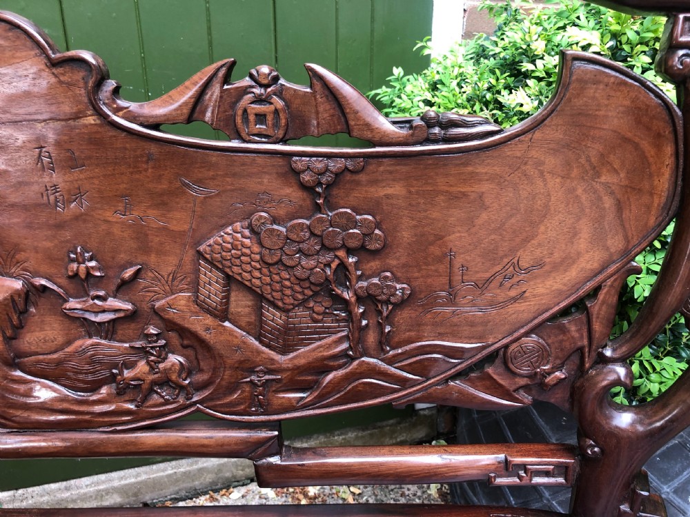 An antique Chinese dark hardwood hall bench featuring detailed relief carvings of bats, landscapes, and traditional character motifs on the backrest. View XXVII