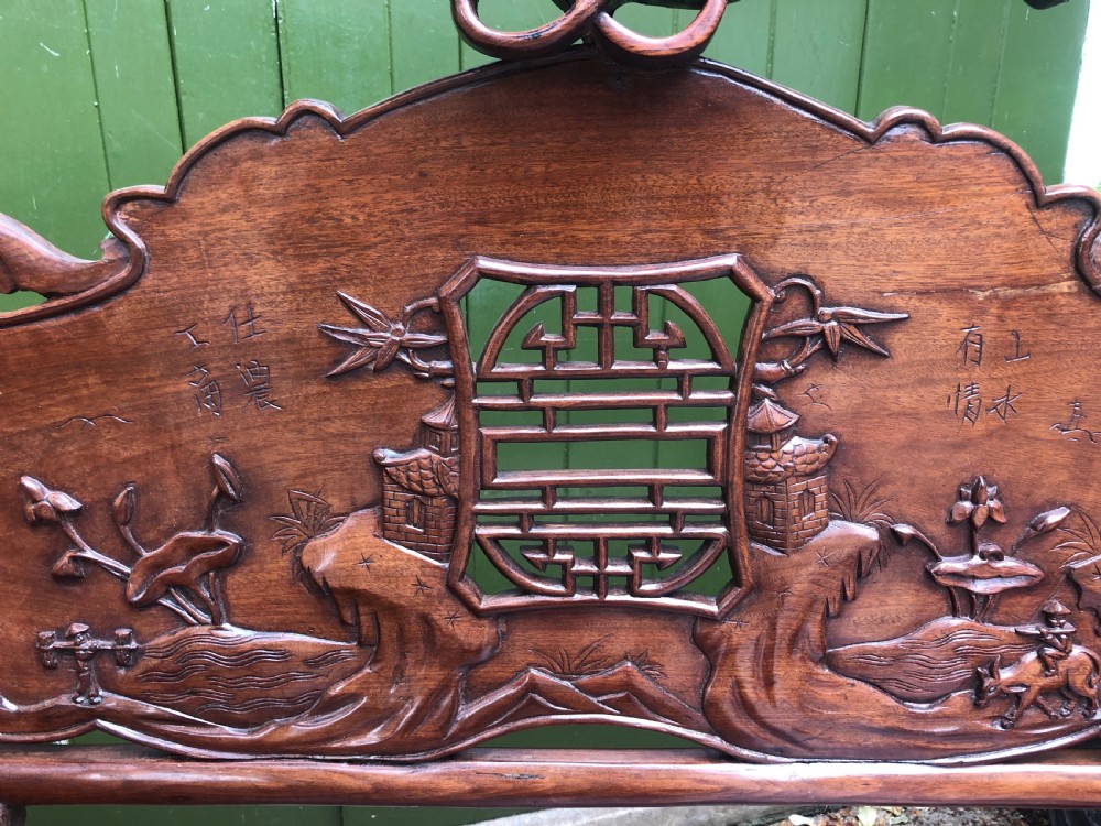 An antique Chinese dark hardwood hall bench featuring detailed relief carvings of bats, landscapes, and traditional character motifs on the backrest. View XXVIII
