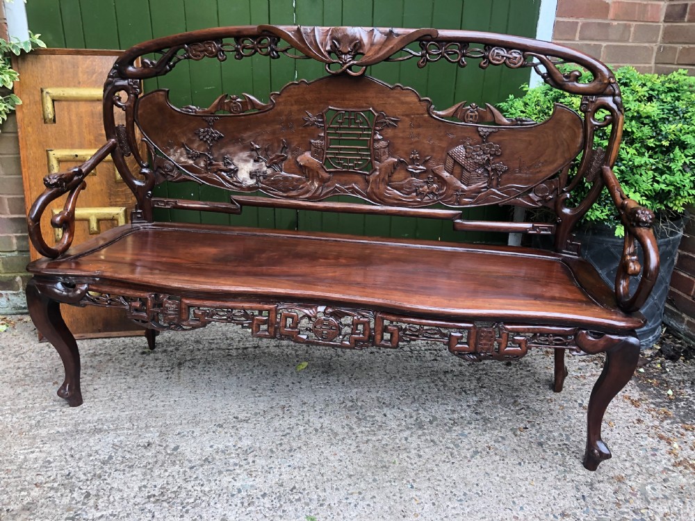 An antique Chinese dark hardwood hall bench featuring detailed relief carvings of bats, landscapes, and traditional character motifs on the backrest. View XXIX