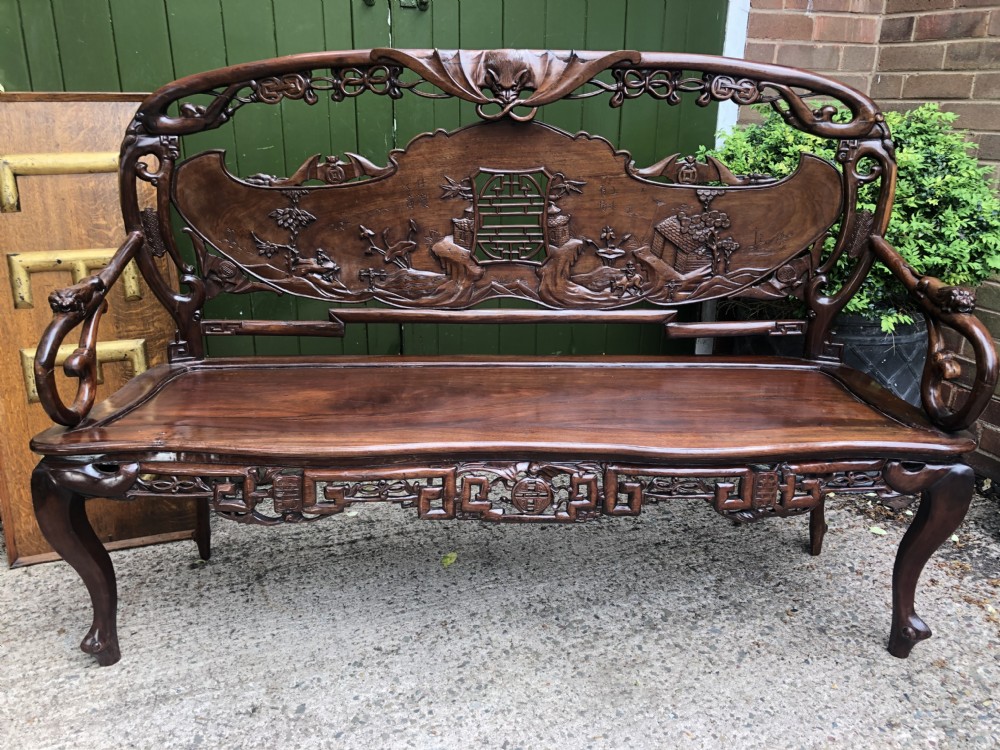 An antique Chinese dark hardwood hall bench featuring detailed relief carvings of bats, landscapes, and traditional character motifs on the backrest.