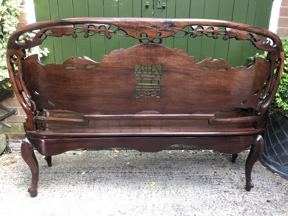 An antique Chinese dark hardwood hall bench featuring detailed relief carvings of bats, landscapes, and traditional character motifs on the backrest. View XV