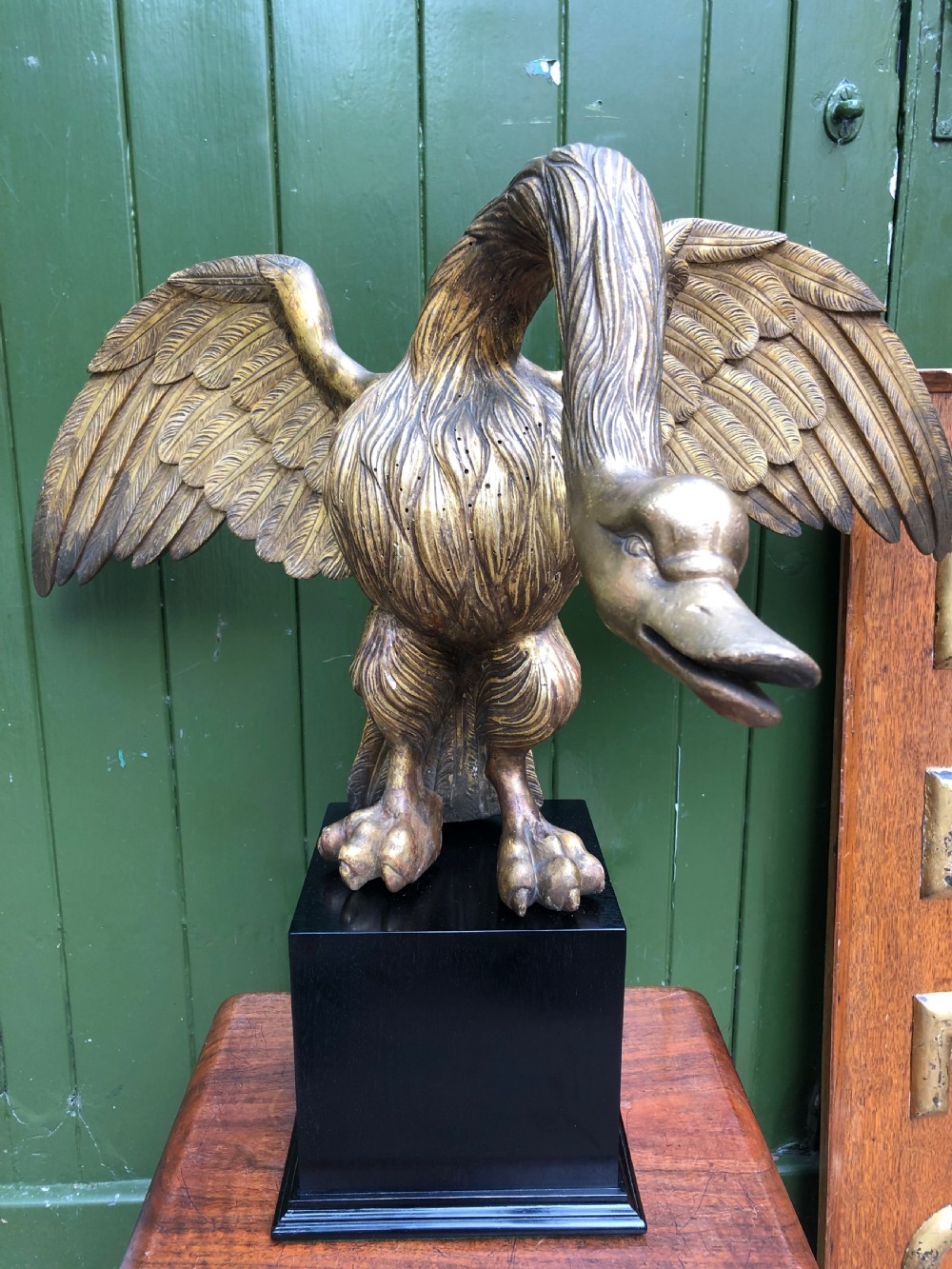 A carved giltwood swan sculpture with outstretched wings and a lowered head mounted on a black square pedestal.