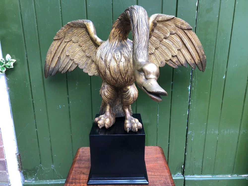A carved giltwood swan sculpture with outstretched wings and a lowered head mounted on a black square pedestal. View III
