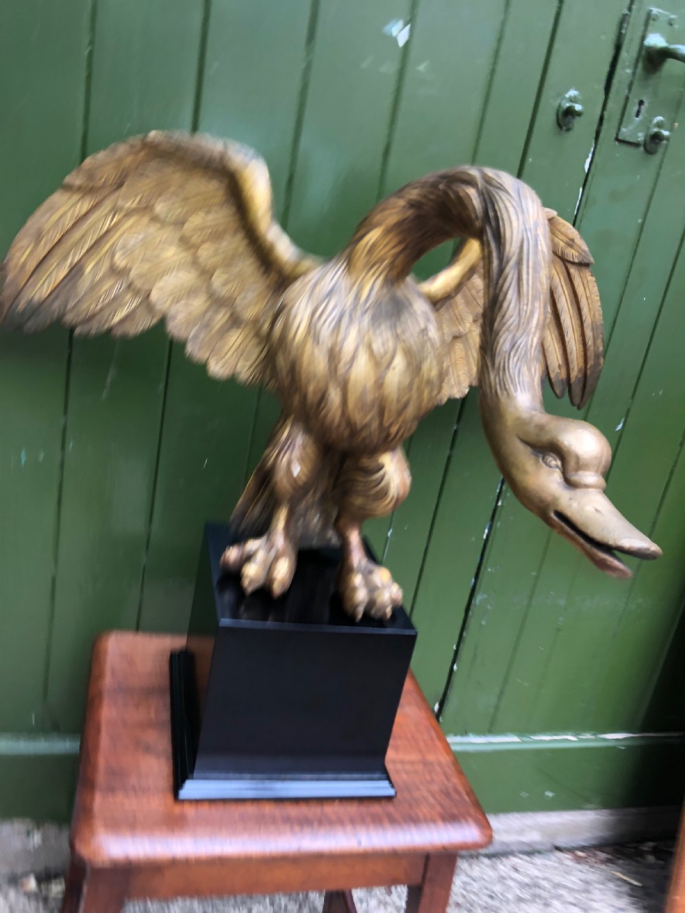 A carved giltwood swan sculpture with outstretched wings and a lowered head mounted on a black square pedestal. View V