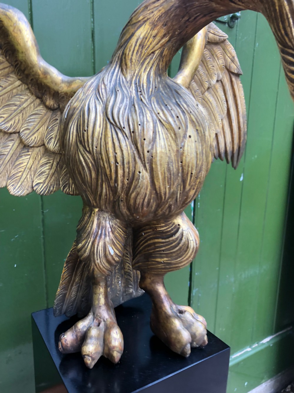 A carved giltwood swan sculpture with outstretched wings and a lowered head mounted on a black square pedestal. View VIII