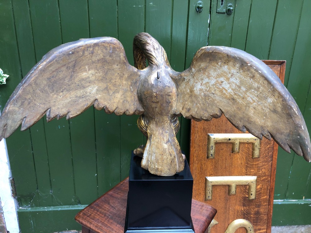 A carved giltwood swan sculpture with outstretched wings and a lowered head mounted on a black square pedestal. View XI
