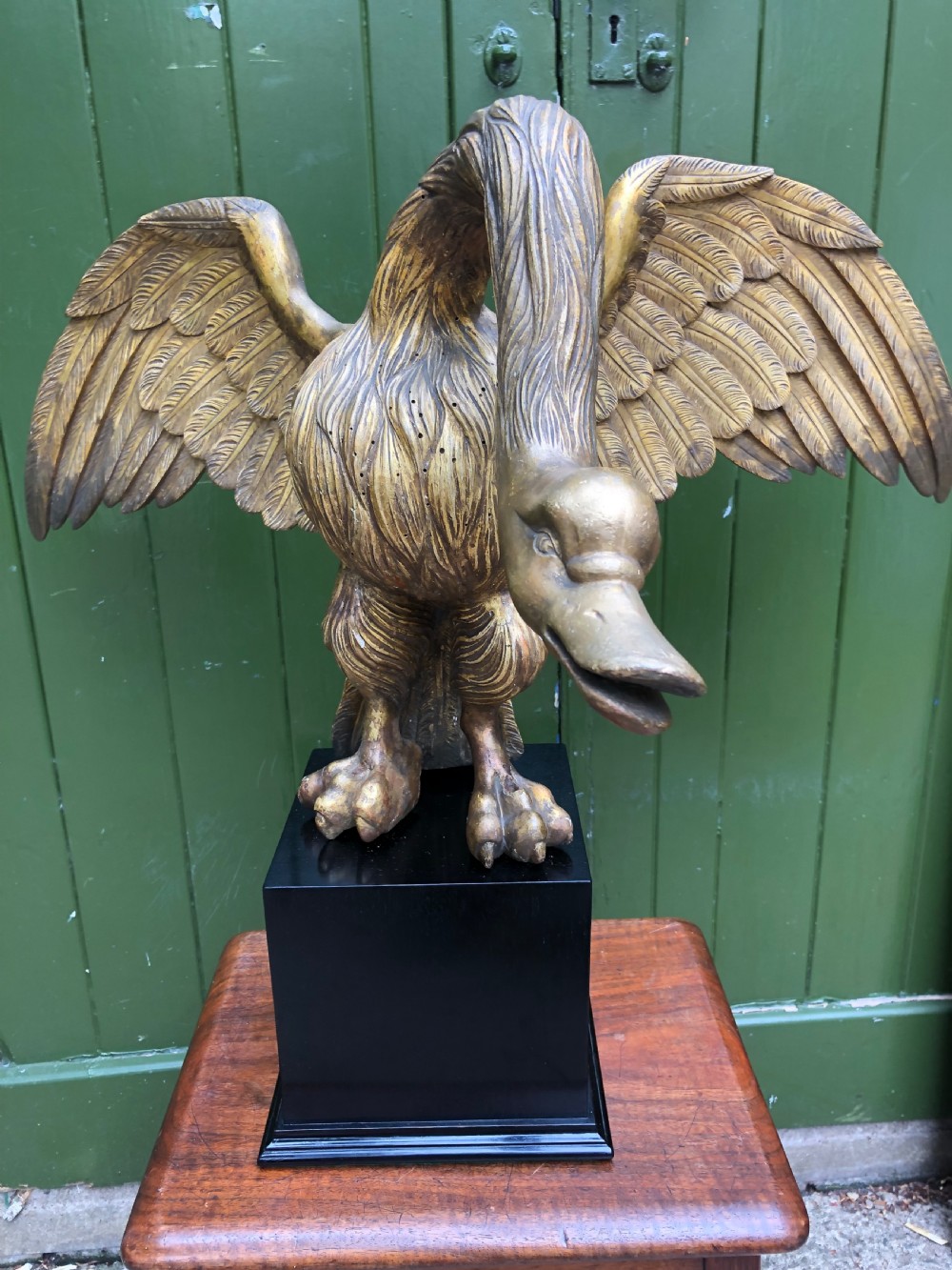 A carved giltwood swan sculpture with outstretched wings and a lowered head mounted on a black square pedestal. View XIII