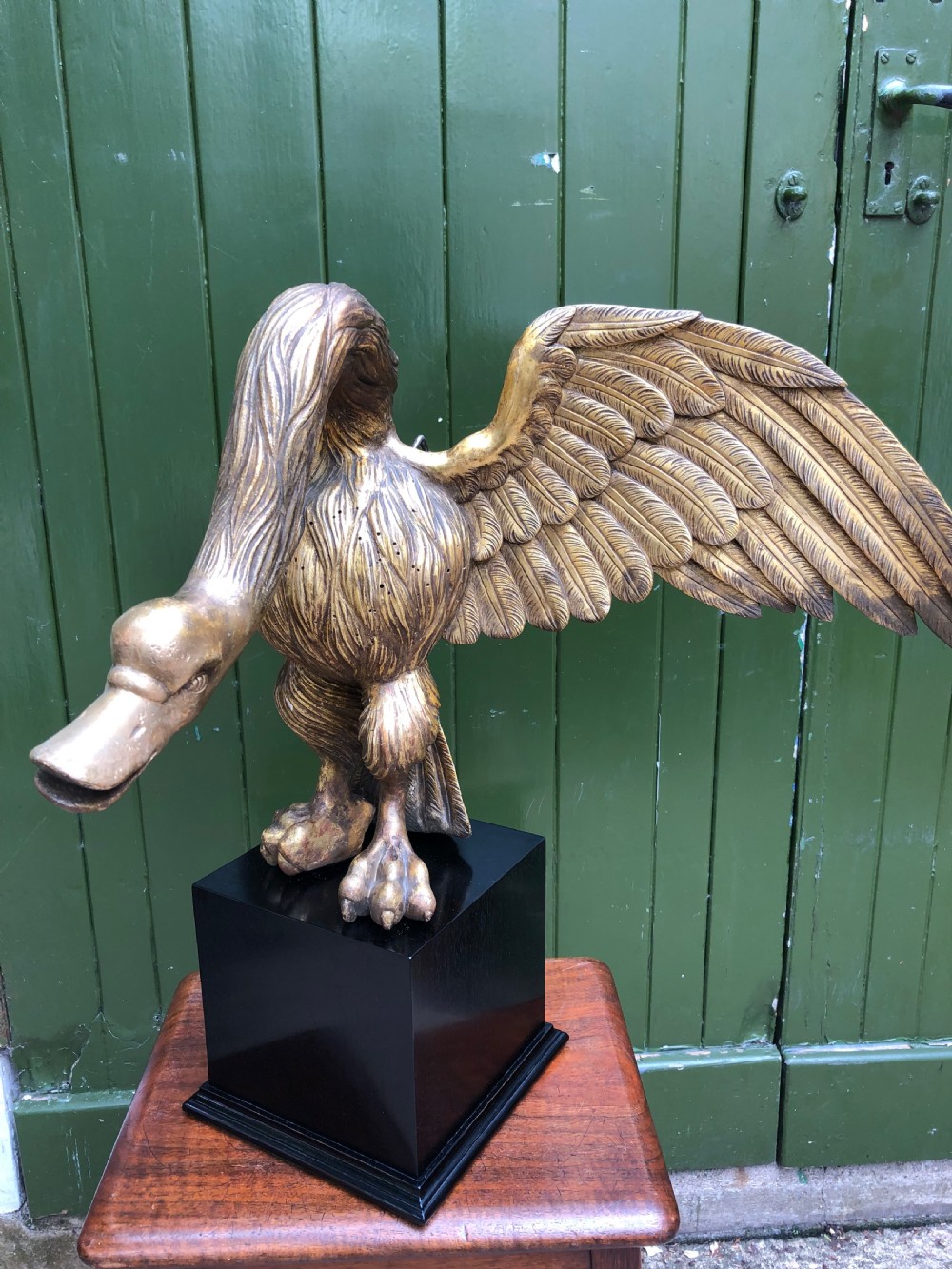 A carved giltwood swan sculpture with outstretched wings and a lowered head mounted on a black square pedestal. View XIV