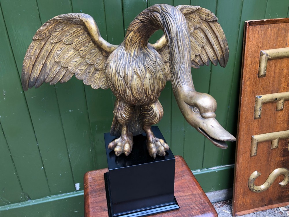 A carved giltwood swan sculpture with outstretched wings and a lowered head mounted on a black square pedestal. View XV