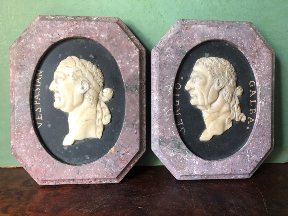 A pair of octagonal mottled pink marble plaques featuring carved off-white marble profile portraits of Roman emperors Vespasian and Galba set against black oval backgrounds.