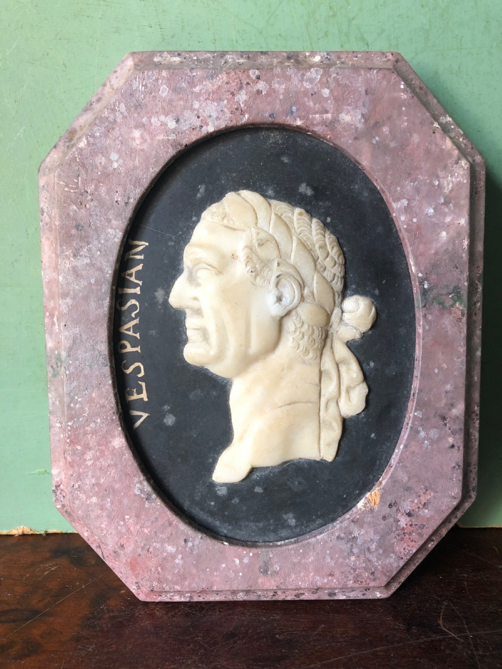A pair of octagonal mottled pink marble plaques featuring carved off-white marble profile portraits of Roman emperors Vespasian and Galba set against black oval backgrounds. View VI