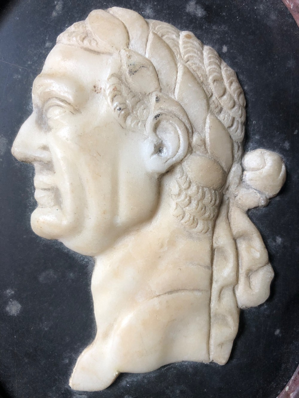 A pair of octagonal mottled pink marble plaques featuring carved off-white marble profile portraits of Roman emperors Vespasian and Galba set against black oval backgrounds. View XII