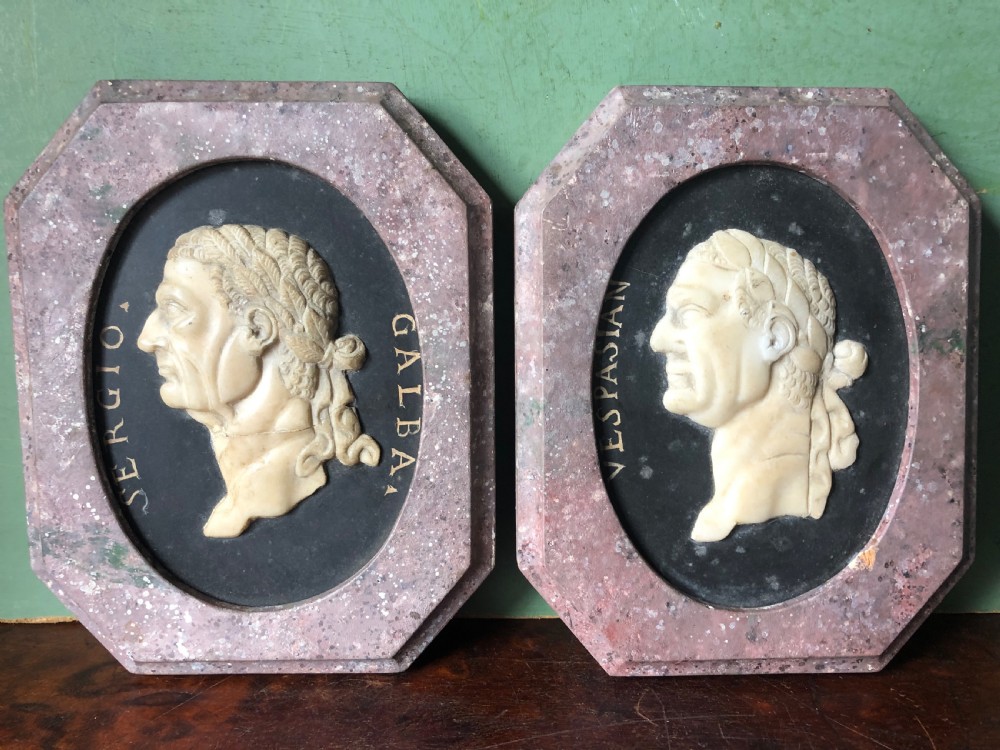 A pair of octagonal mottled pink marble plaques featuring carved off-white marble profile portraits of Roman emperors Vespasian and Galba set against black oval backgrounds. View XVI