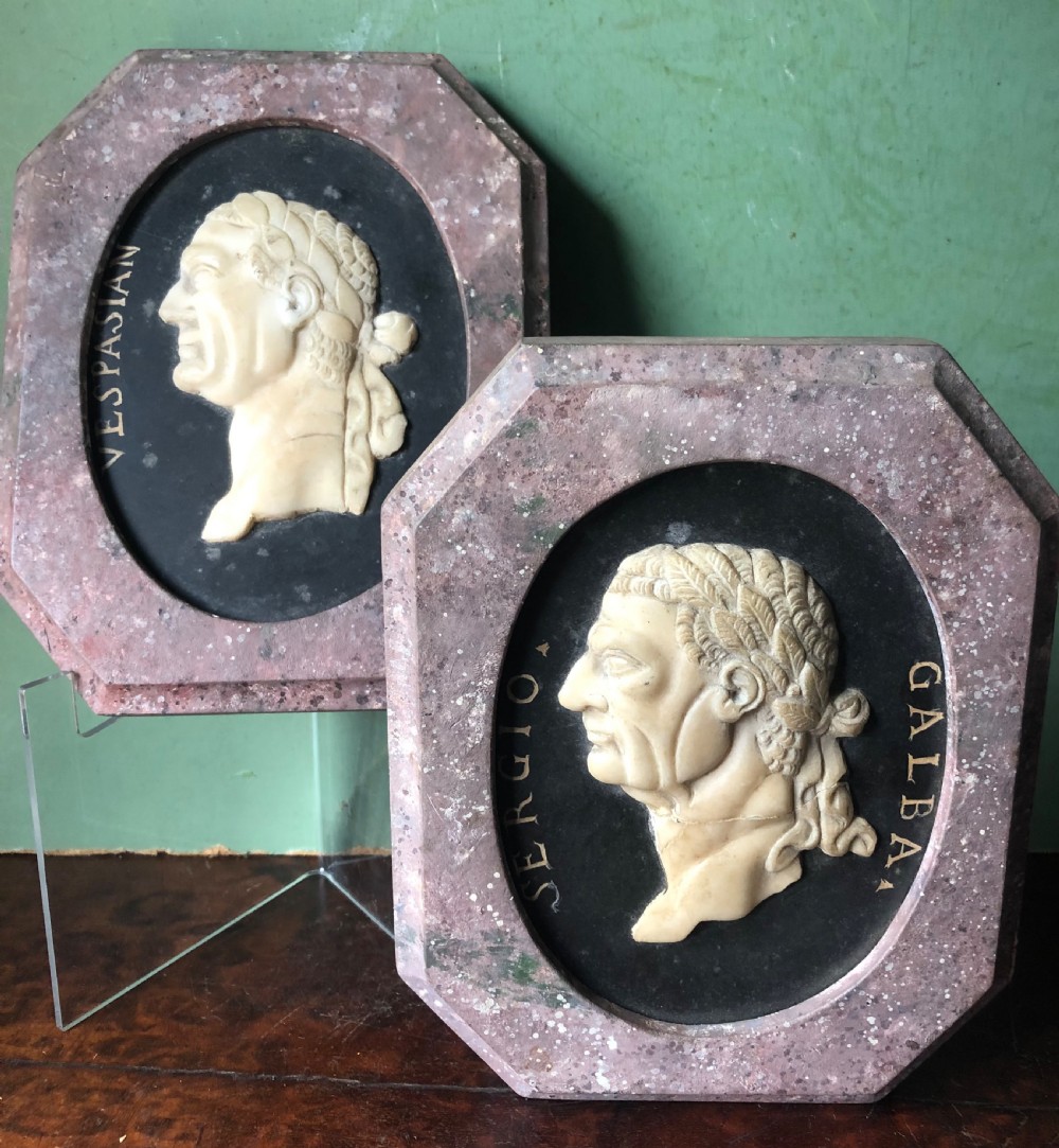 A pair of octagonal mottled pink marble plaques featuring carved off-white marble profile portraits of Roman emperors Vespasian and Galba set against black oval backgrounds. View XVII