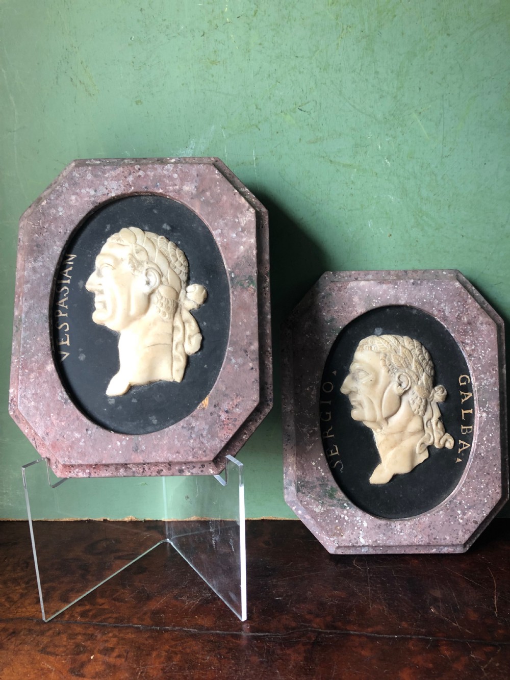 A pair of octagonal mottled pink marble plaques featuring carved off-white marble profile portraits of Roman emperors Vespasian and Galba set against black oval backgrounds. View XVIII