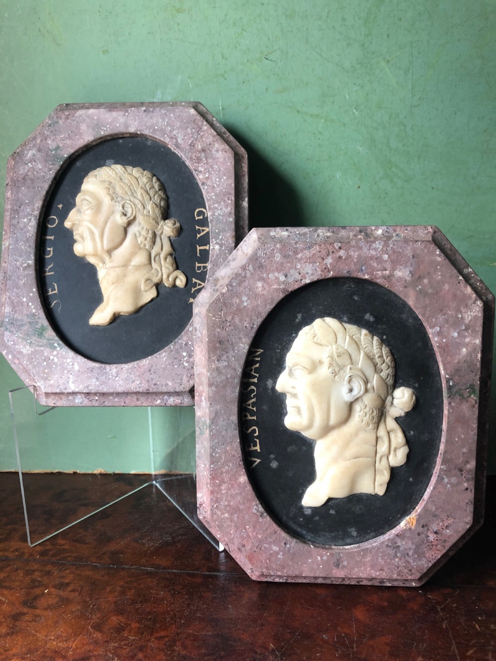 A pair of octagonal mottled pink marble plaques featuring carved off-white marble profile portraits of Roman emperors Vespasian and Galba set against black oval backgrounds. View XIX