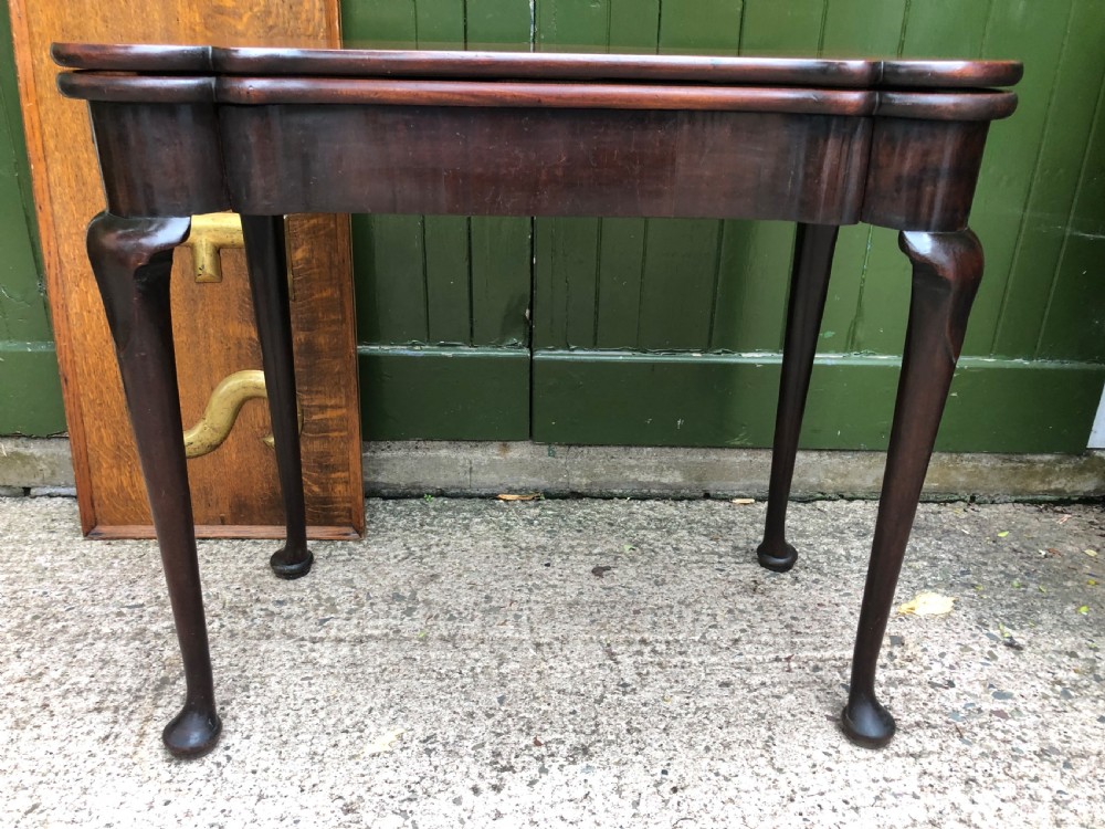 A mid-18th-century George II mahogany fold-over card table featuring slender cabriole legs terminating in pad feet and a shaped top.