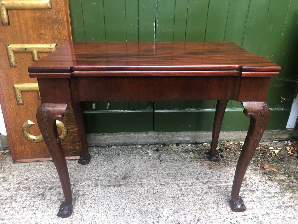 A mid-18th-century George II mahogany fold-over card table featuring carved cabriole legs and claw and ball feet.