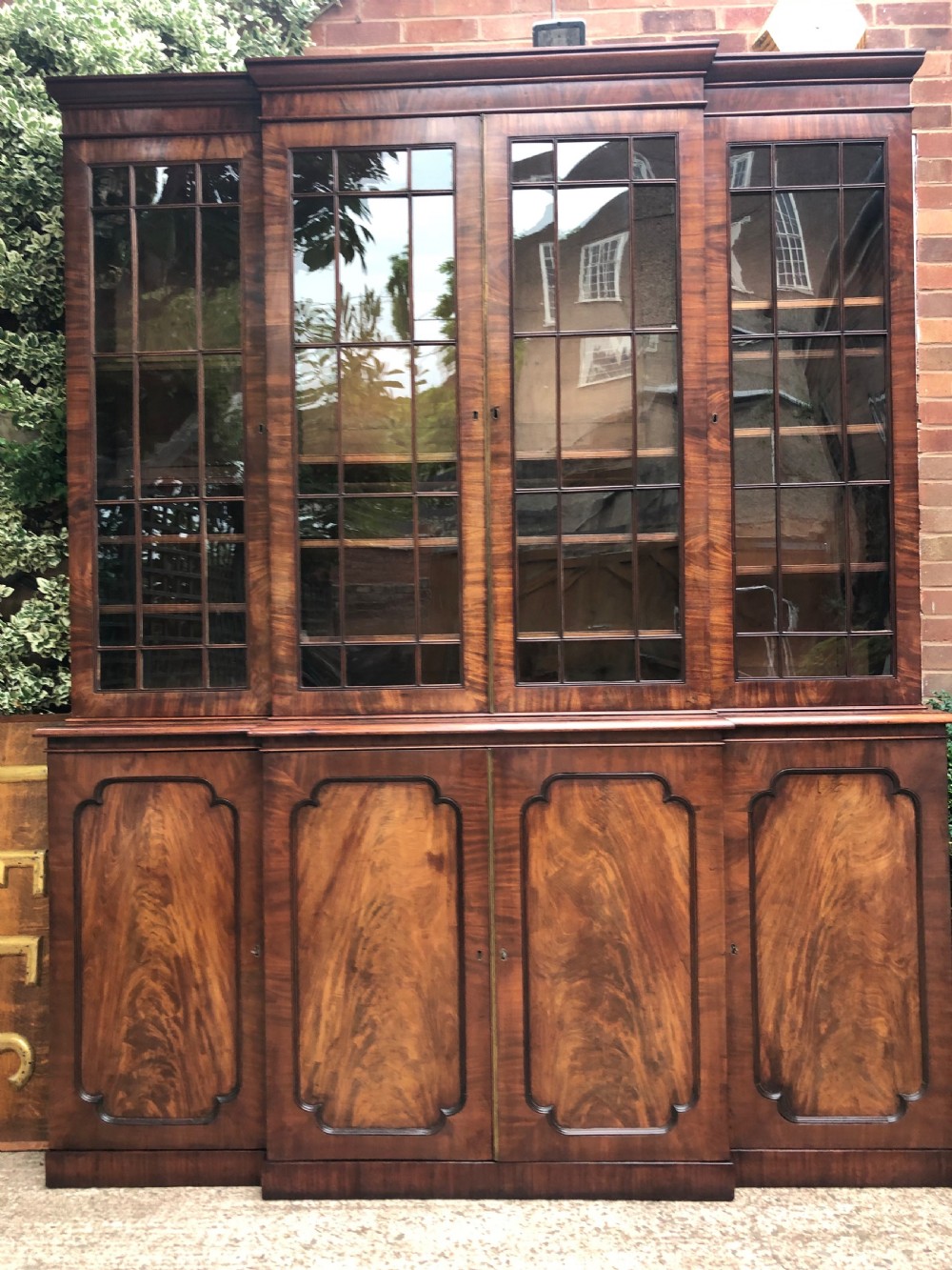 An early 19th-century George IV flame mahogany breakfront library bookcase featuring four upper glazed doors with astragal glazing bars above four fielded panel lower cupboards. View II