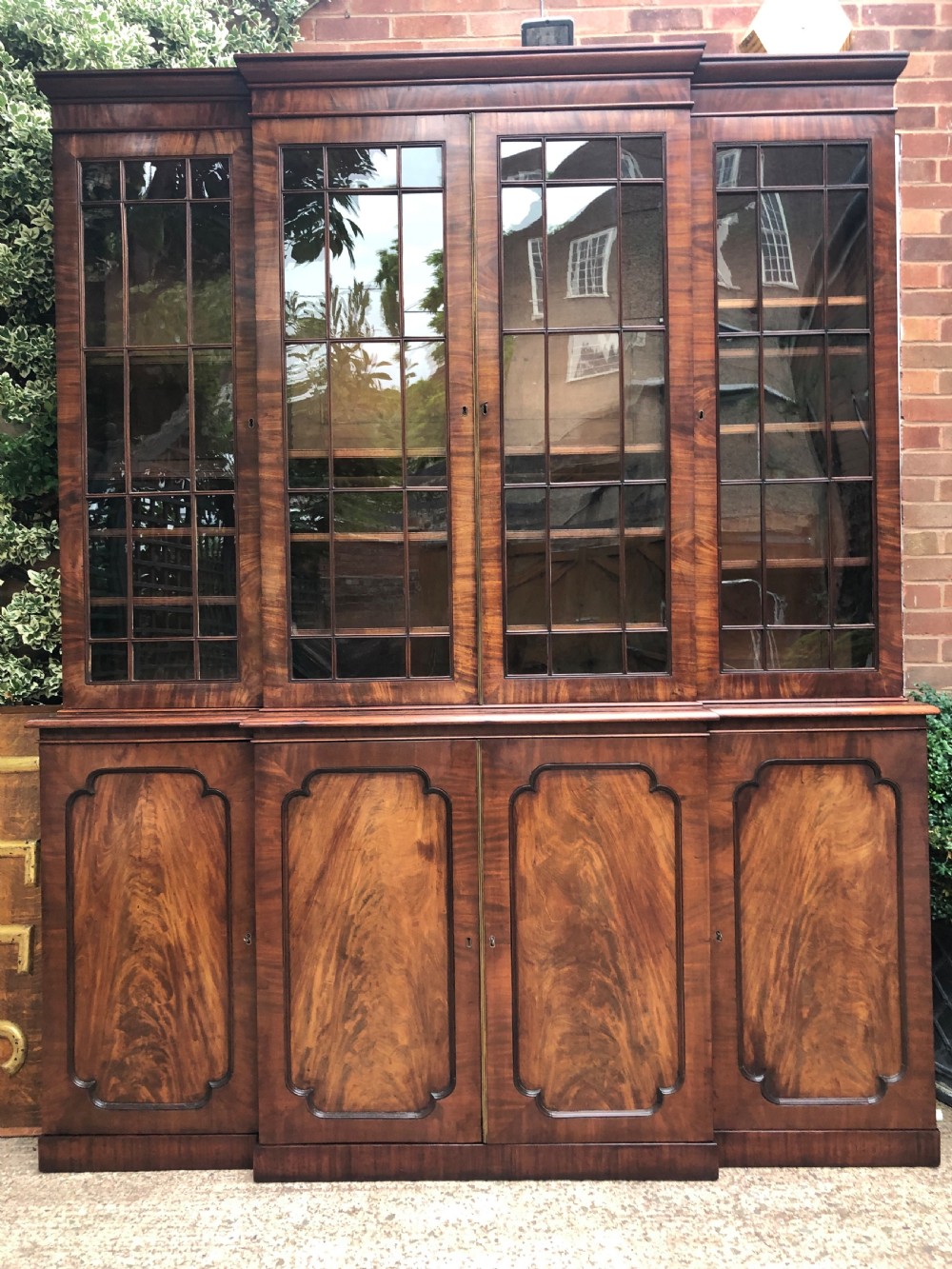 An early 19th-century George IV flame mahogany breakfront library bookcase featuring four upper glazed doors with astragal glazing bars above four fielded panel lower cupboards. View III