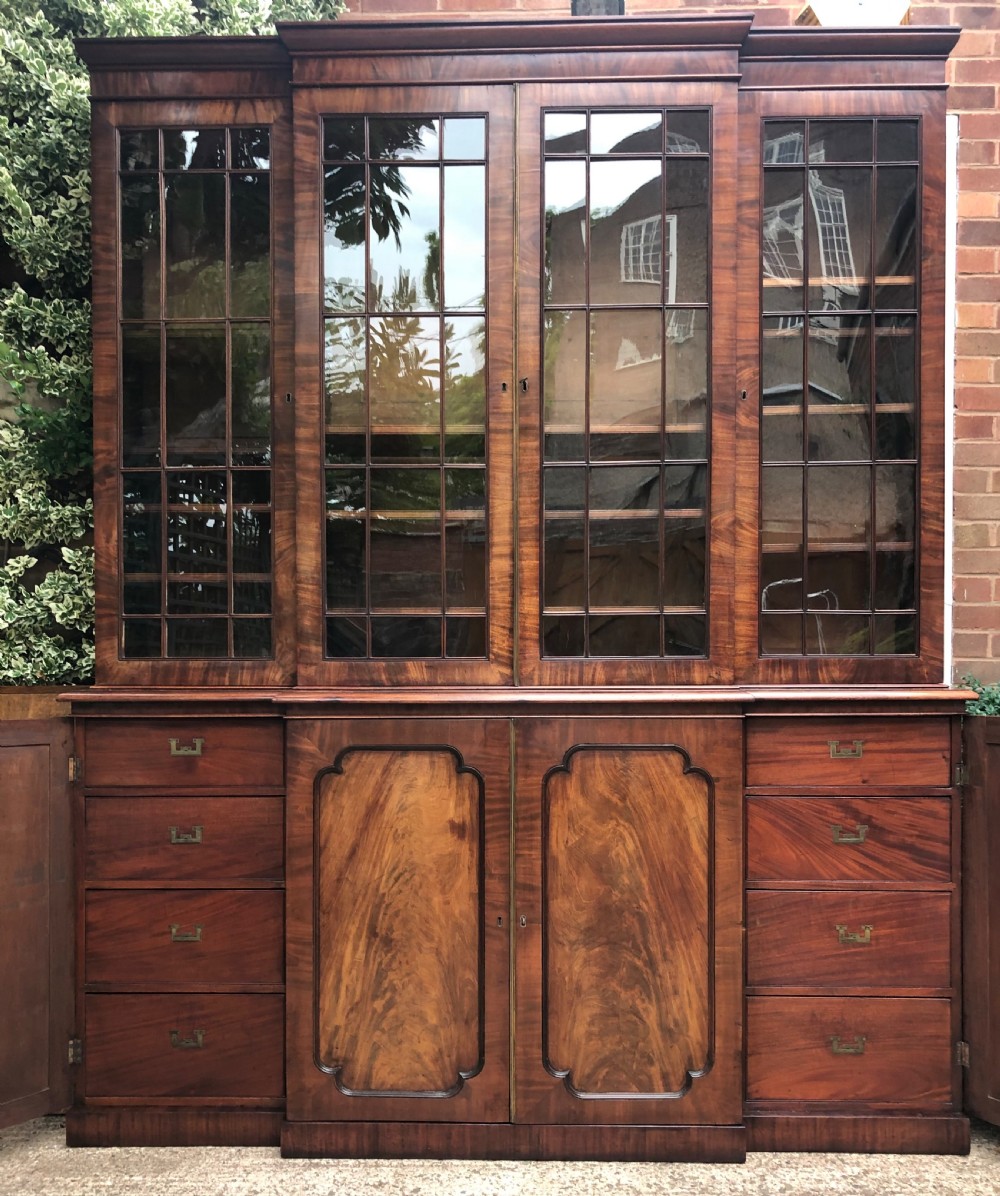 An early 19th-century George IV flame mahogany breakfront library bookcase featuring four upper glazed doors with astragal glazing bars above four fielded panel lower cupboards. View VI