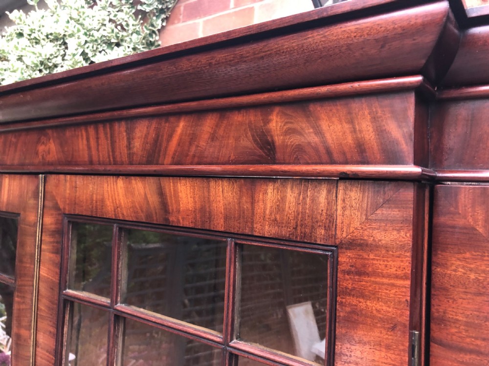 An early 19th-century George IV flame mahogany breakfront library bookcase featuring four upper glazed doors with astragal glazing bars above four fielded panel lower cupboards. View XIII