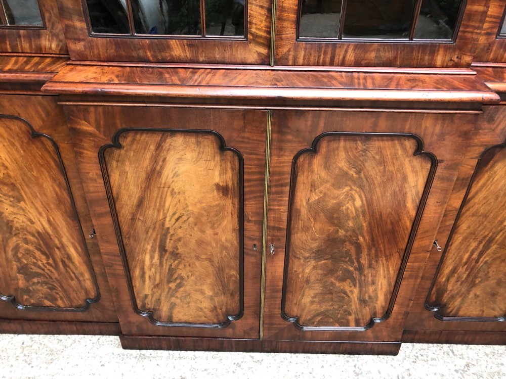An early 19th-century George IV flame mahogany breakfront library bookcase featuring four upper glazed doors with astragal glazing bars above four fielded panel lower cupboards. View XIV