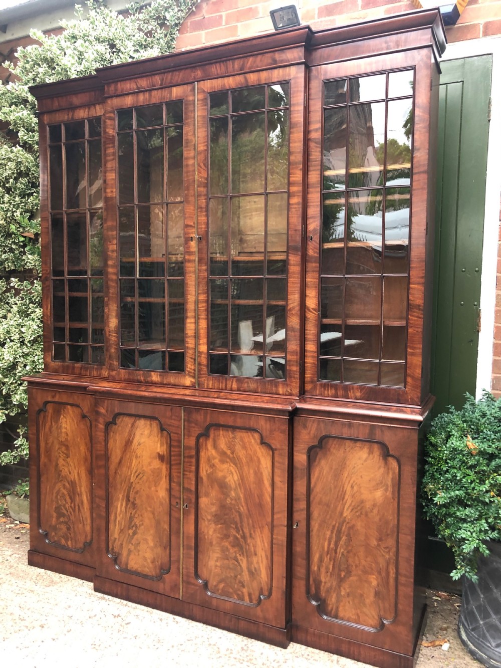 An early 19th-century George IV flame mahogany breakfront library bookcase featuring four upper glazed doors with astragal glazing bars above four fielded panel lower cupboards. View XVI