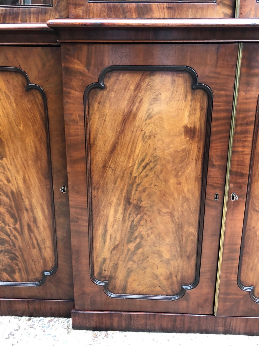 An early 19th-century George IV flame mahogany breakfront library bookcase featuring four upper glazed doors with astragal glazing bars above four fielded panel lower cupboards. View XXII