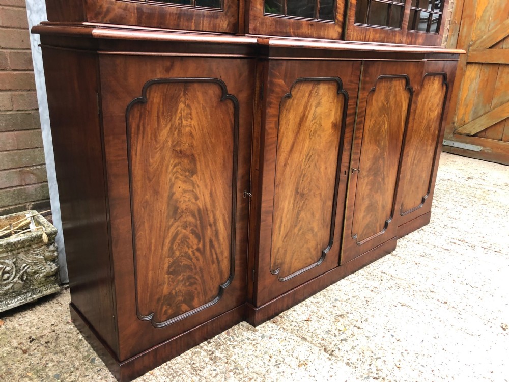 An early 19th-century George IV flame mahogany breakfront library bookcase featuring four upper glazed doors with astragal glazing bars above four fielded panel lower cupboards. View XXV
