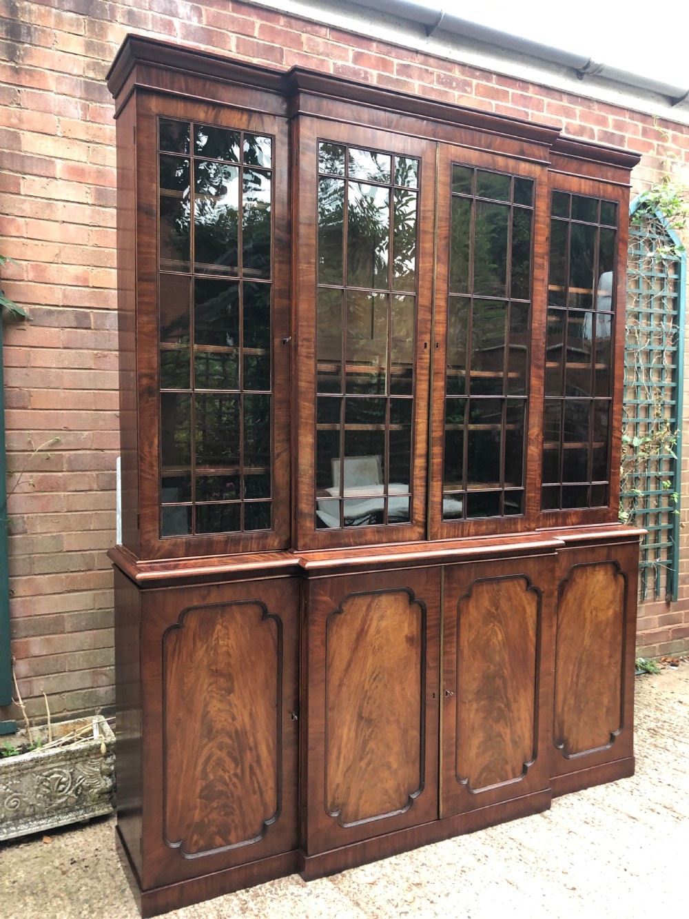An early 19th-century George IV flame mahogany breakfront library bookcase featuring four upper glazed doors with astragal glazing bars above four fielded panel lower cupboards. View XXVIII