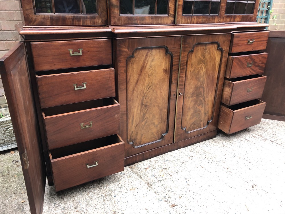 An early 19th-century George IV flame mahogany breakfront library bookcase featuring four upper glazed doors with astragal glazing bars above four fielded panel lower cupboards. View V